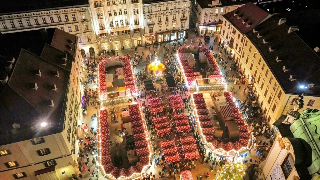 The Christmas market on Bratislava's Main Square seen from above at night, its red and white stalls filling the square around a lit carousel.