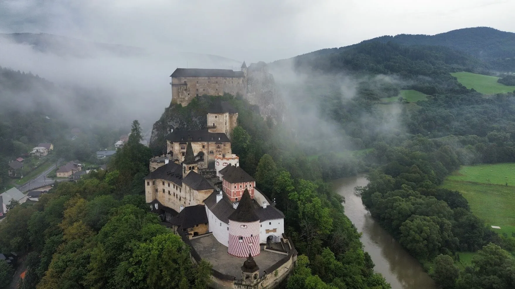 Orava Castle rising on its rock above the river, seen from the air through morning mist.