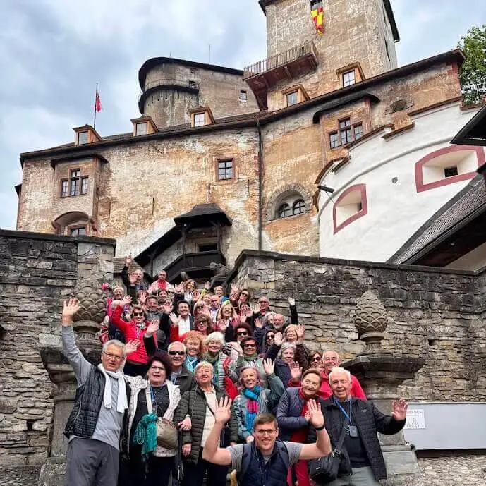 Eine große Reisegruppe winkt von den Stufen unterhalb der Burg Orava in der Slowakei.