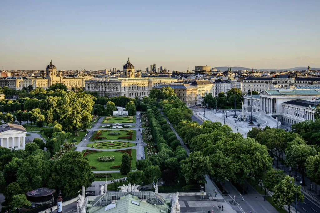 Wien von oben bei Sonnenuntergang, mit Blick über die Gärten und die großen Museumsbauten der Ringstraße.
