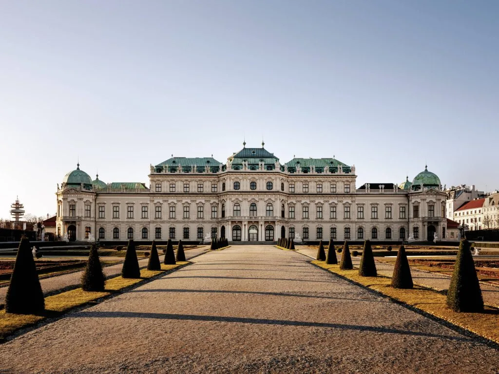 The Upper Belvedere palace in Vienna seen along the garden path, with clipped conical yews on either side.