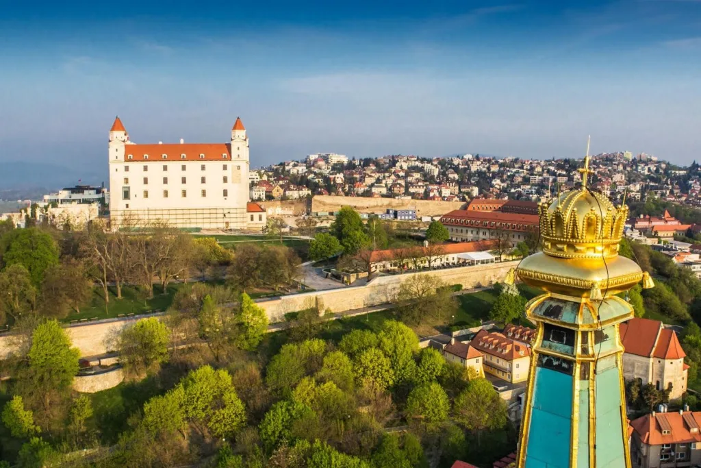 Bratislava Castle standing white above the trees, seen across the rooftops of the old town.