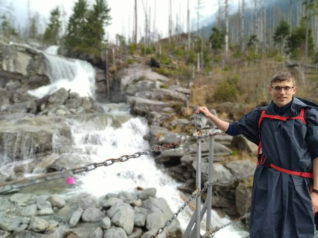A visitor beside a mountain stream falling over boulders in the High Tatras, a chain handrail along the path.