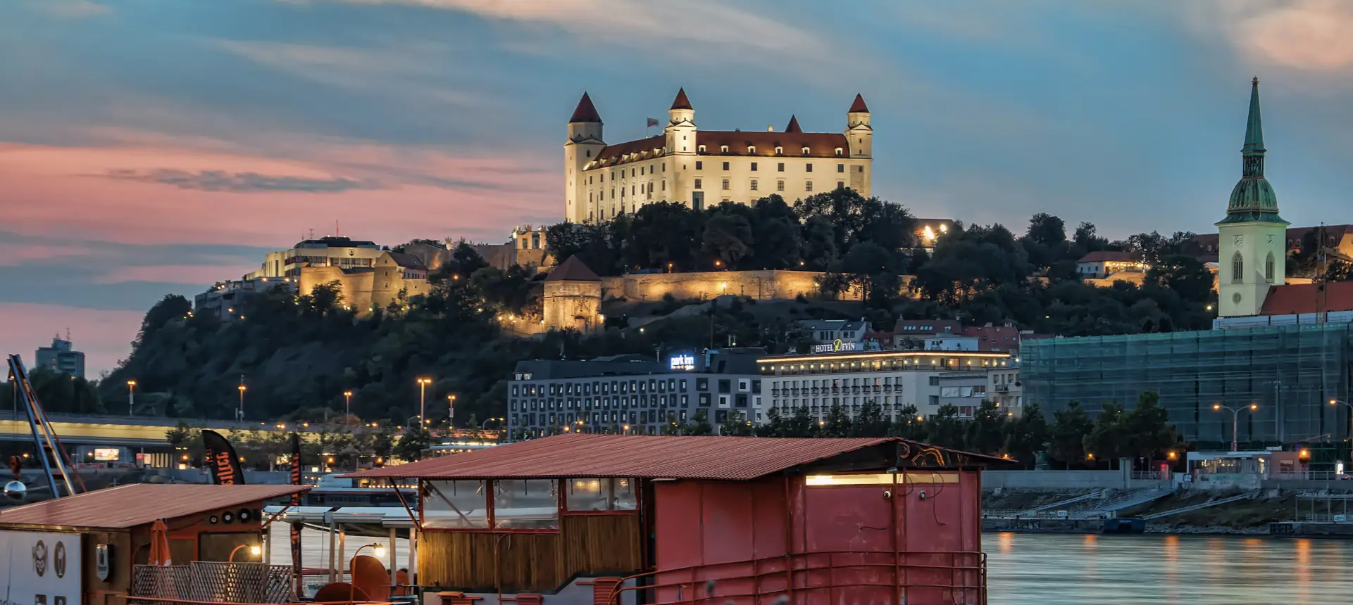 Die Burg Bratislava und der Martinsdom, über der Donau in der Abenddämmerung beleuchtet.