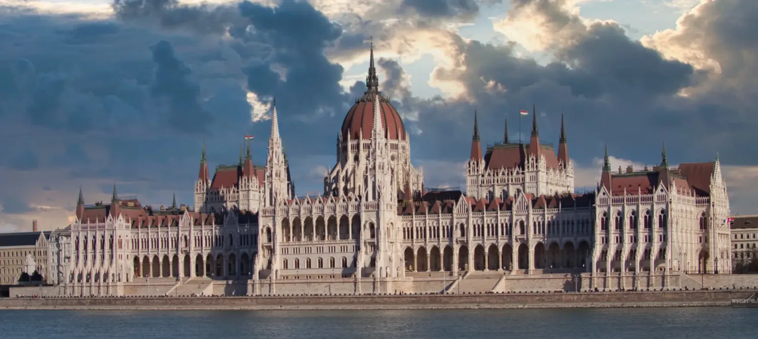 Das ungarische Parlament am Donauufer in Budapest unter dramatischem Himmel.