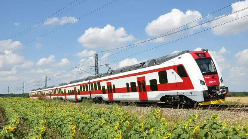 Ein rot-weißer slowakischer Regionalzug fährt an einem Sommertag an einem Sonnenblumenfeld vorbei.