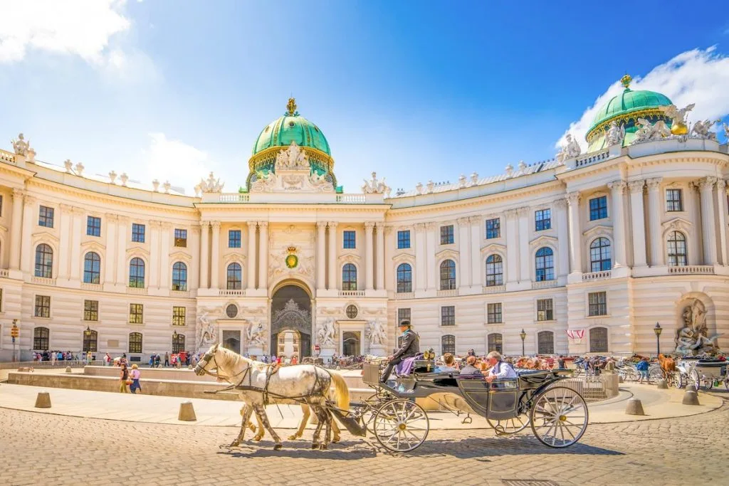 A fiaker carriage crossing Michaelerplatz in Vienna in front of the domed Michaeler wing of the Hofburg.