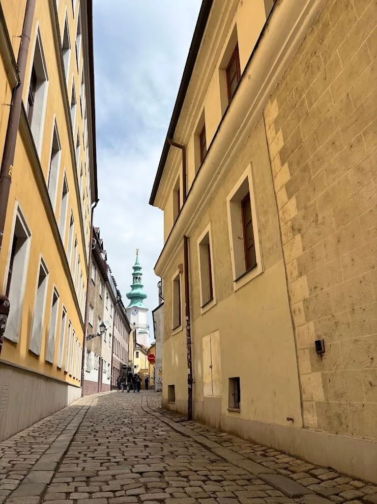 Eine schmale Kopfsteinpflastergasse in der Altstadt von Bratislava, die zum grünen Turm des Michaelertors führt.