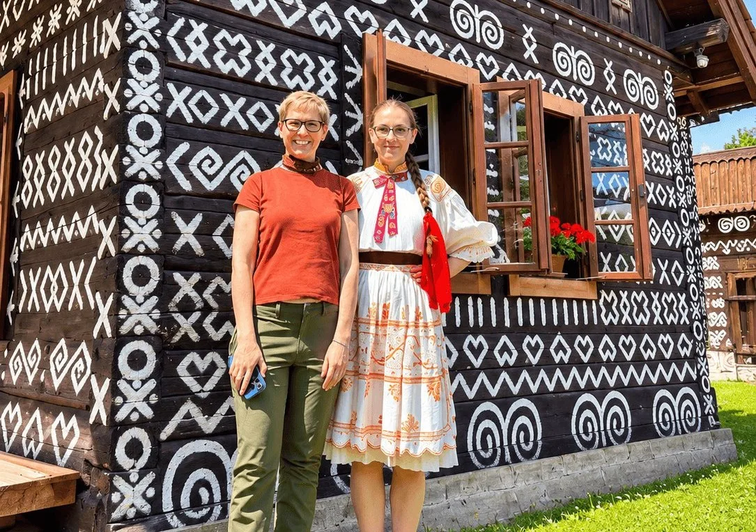 A visitor and a woman in traditional Slovak folk dress outside a painted wooden house in Čičmany.