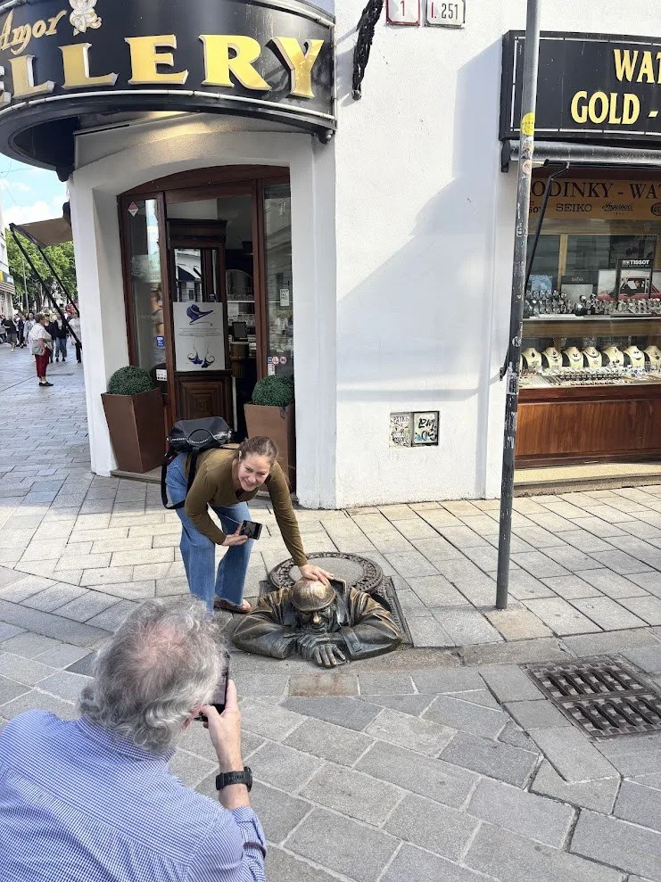 Visitors photographing the Cumil bronze statue peering out of a manhole in Bratislava's old town.