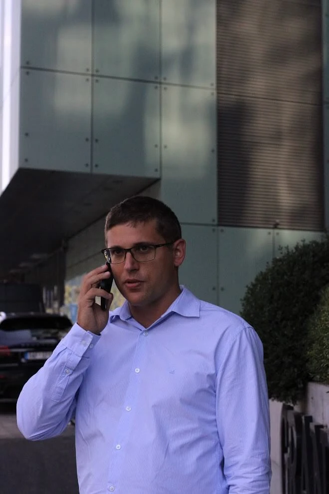 Andrej Stanik on a phone call outside a modern office building.