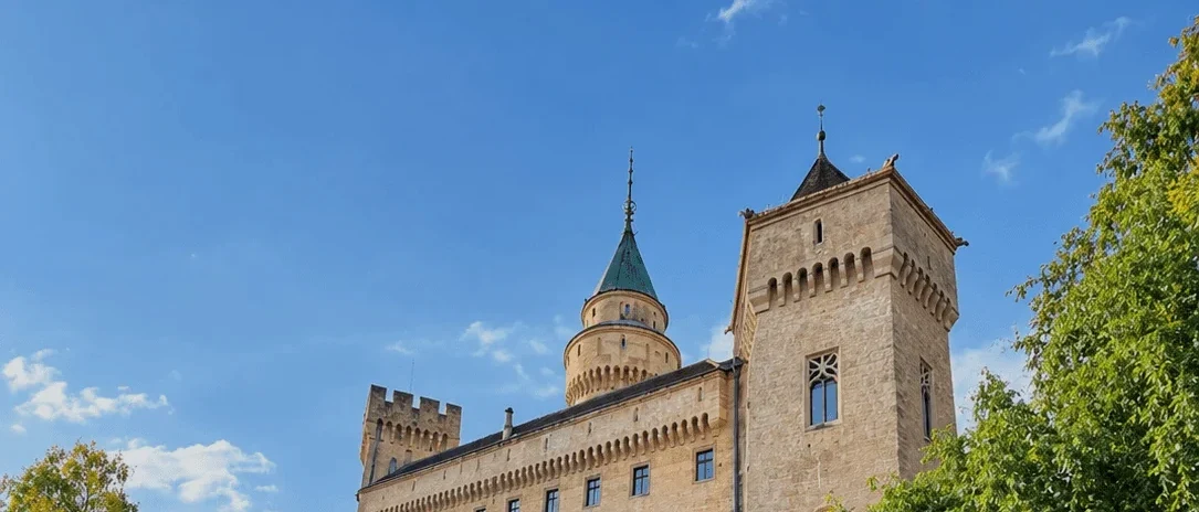 Bojnice Castle above its ivy-covered wall, the green-roofed round tower and the stone gate tower against a blue autumn sky.