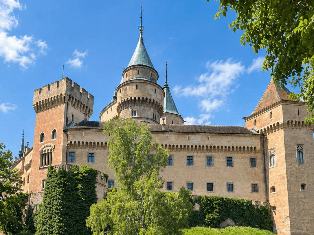 Bojnice Castle in central Slovakia, its towers and turrets rising above the castle gardens on a sunny day.