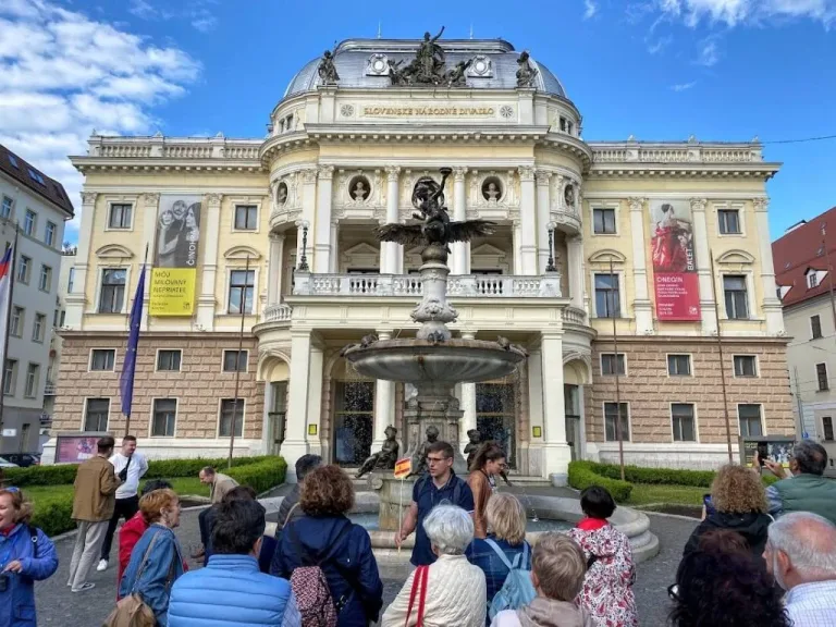 Un grupo turístico escuchando a su guía frente al histórico edificio del Teatro Nacional Eslovaco en Bratislava.