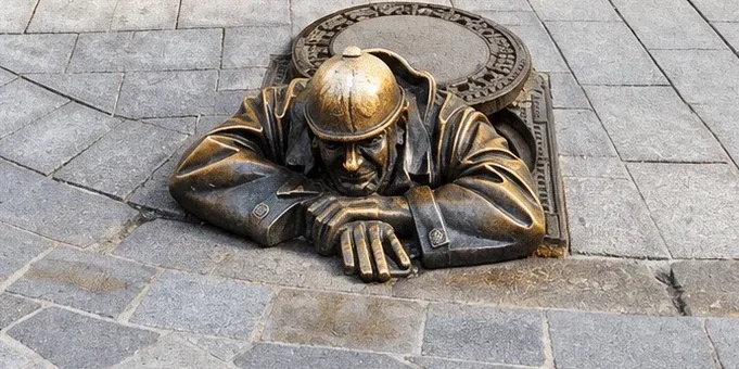 Čumil, die Bronzestatue „Mann bei der Arbeit“, lehnt sich aus einem Kanalschacht in der Kopfsteinpflastergasse der Altstadt von Bratislava.