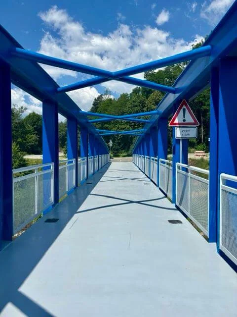 The deck of a blue steel cycle bridge, empty and running straight ahead over the river.