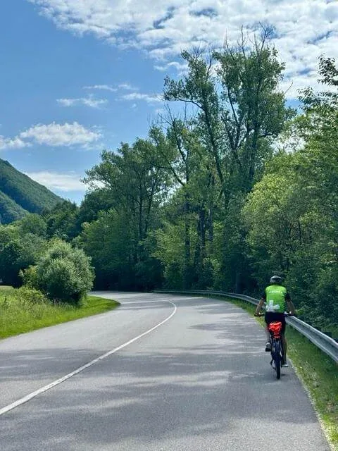 A cyclist in a green jersey riding a quiet road curving through wooded hills in Slovakia.