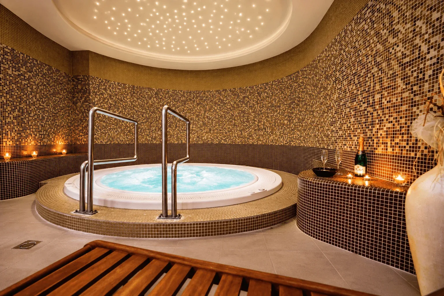 A whirlpool in a mosaic-tiled spa room in Dudince, lit by candles under a starlit ceiling.