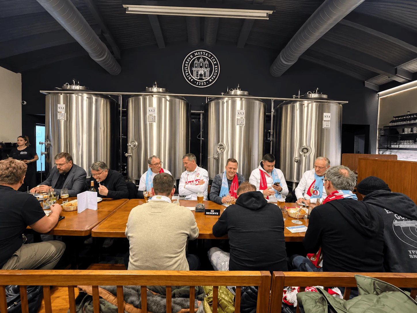 A group at a long table in the brewhouse of the Bratislava Burghers’ Brewery (Bratislavský meštiansky pivovar), with its steel brewing tanks behind them.