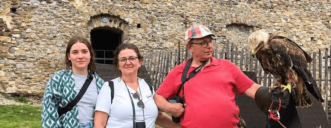 Three visitors beside a falconer holding an eagle on his glove, in front of the stone walls of a castle in Slovakia.