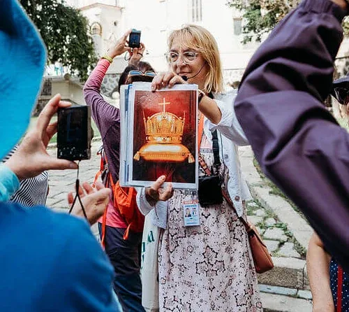 A guide showing a group a picture of the Hungarian Holy Crown during a walking tour in Bratislava Old Town, beside a Gothic church.