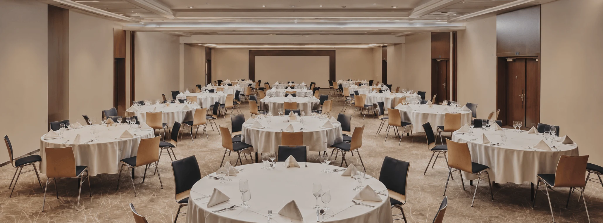 A hotel ballroom set up for a gala dinner, with round tables dressed in white linen and glassware.