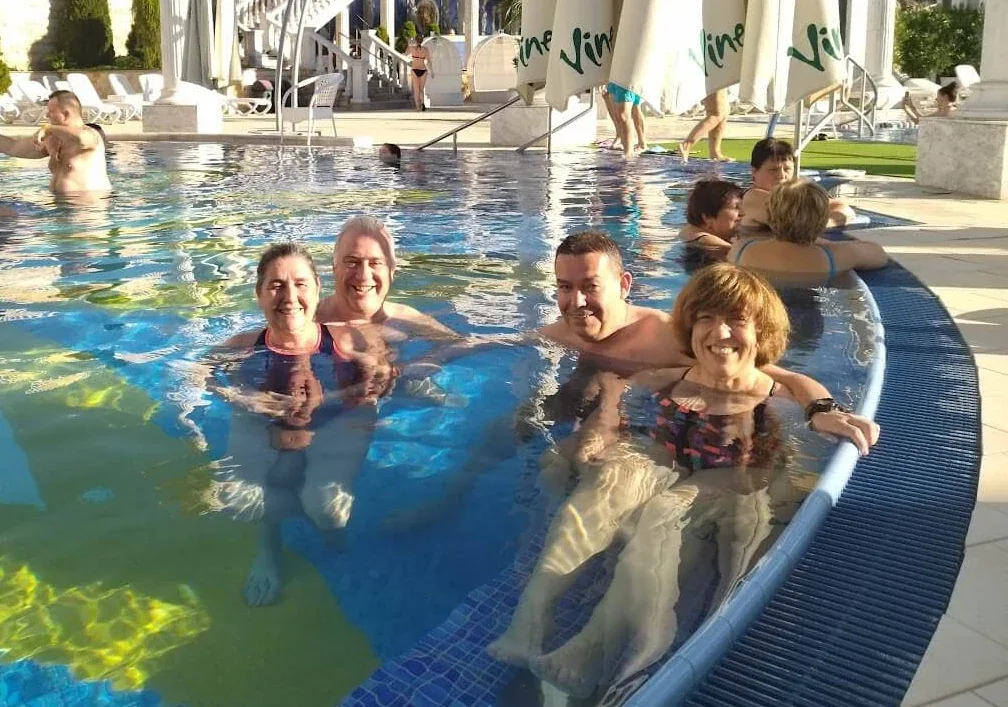 Guests relaxing in the outdoor thermal pool at the Aphrodite spa in Rajecké Teplice, among white columns and balustrades.