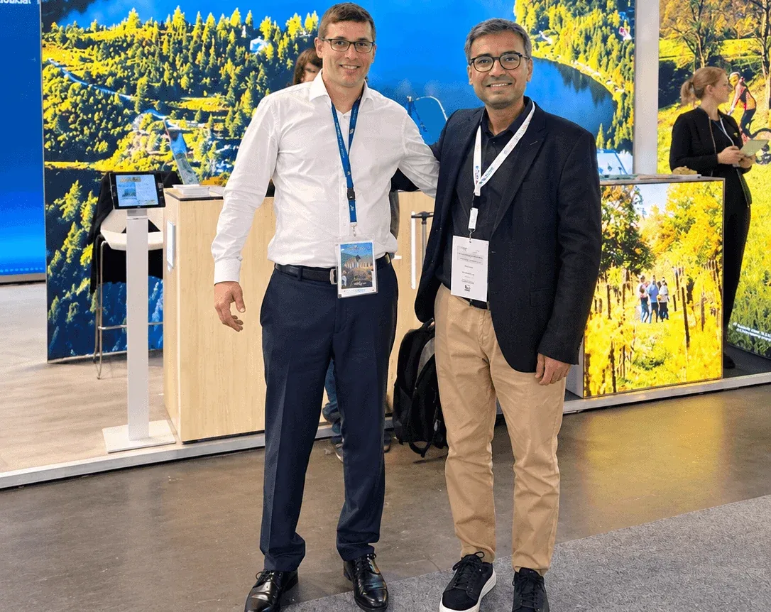 Two people at the Slovakia stand at a travel trade fair, in front of a large photo of a mountain lake.