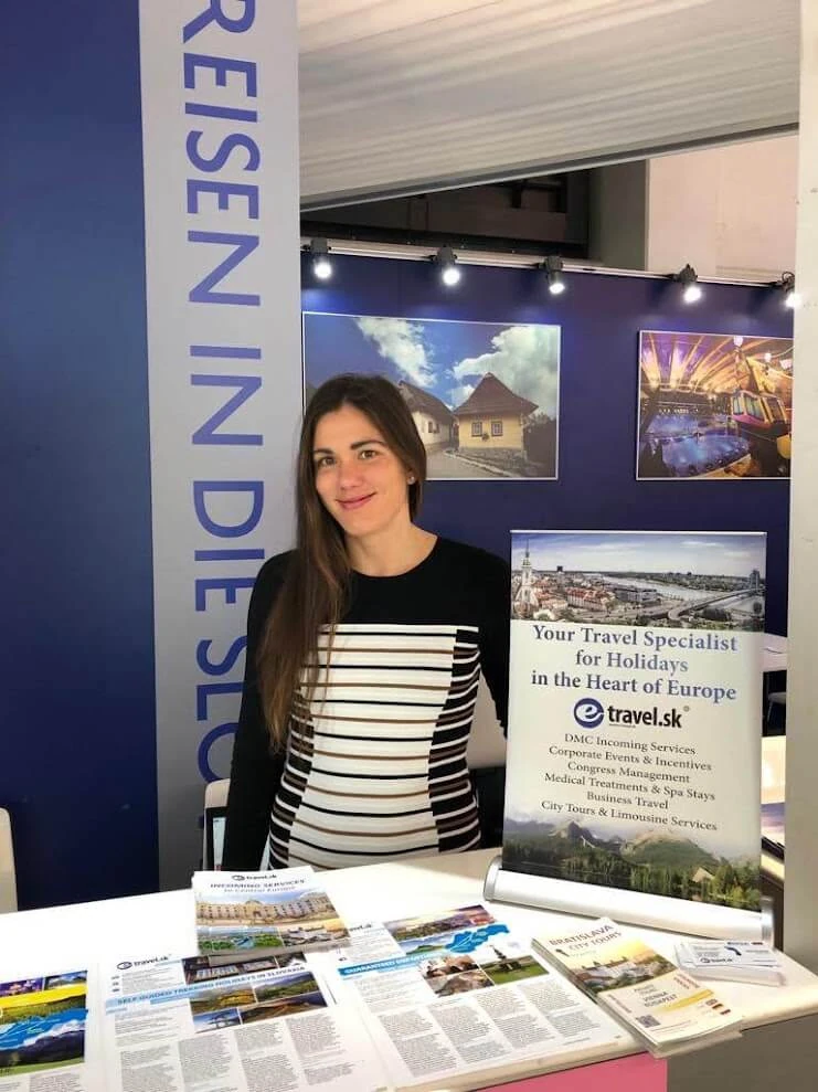 An e-travel.sk travel specialist at the company's stand at a travel trade fair, beside a banner listing its DMC, incentive, congress and spa services.
