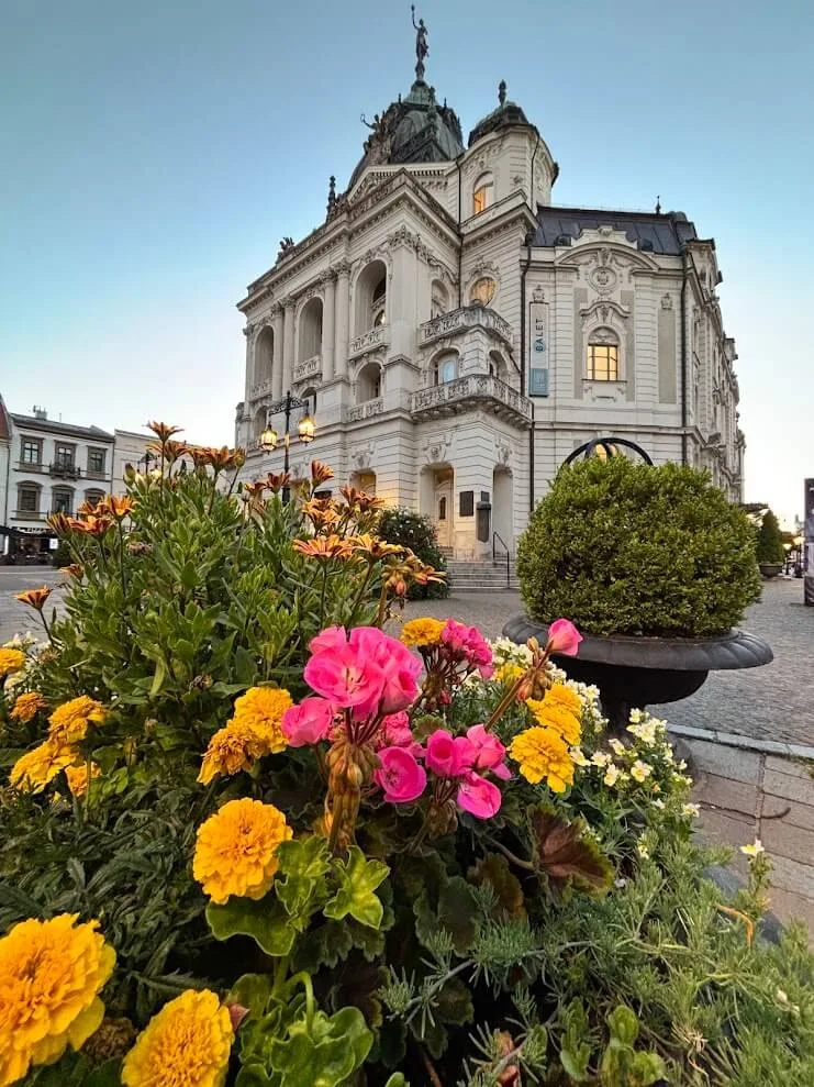 The State Theatre in Košice at dusk, seen across a flower bed on the main square.
