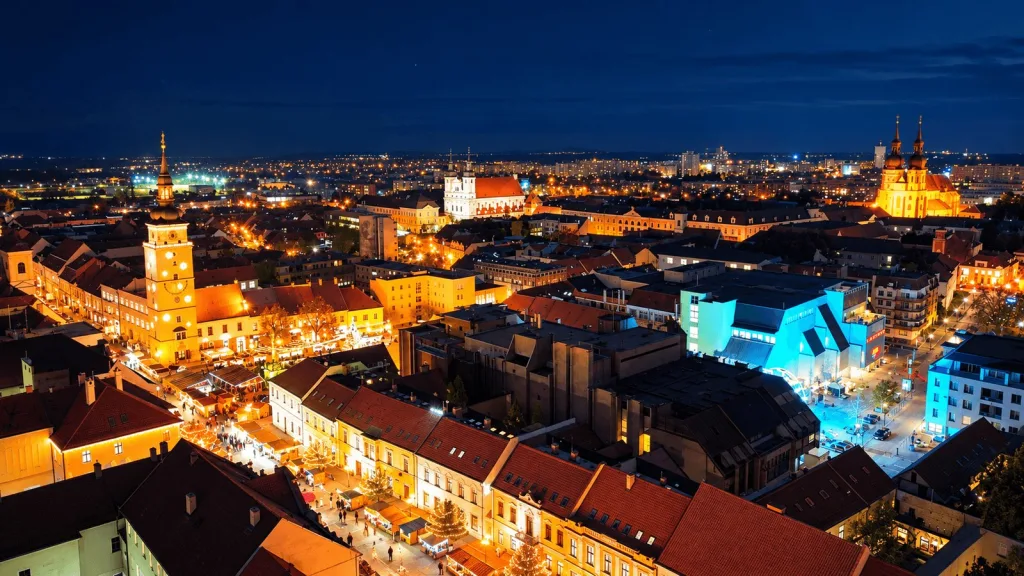 Trnava old town from above at night, with the lit town tower, church spires and market stalls on the main square.