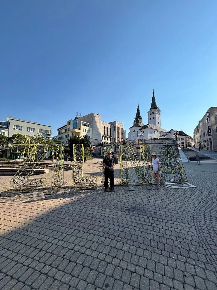 Visitors beside the ZILINA letters on the main square, with the twin towers of the parish church behind.