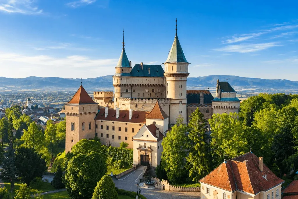 Bojnice Castle from the air, its turrets and green roofs above the park, with the town and the hills of the Upper Nitra valley beyond.