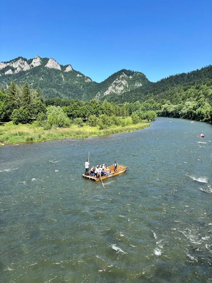 A wooden raft carrying passengers down the Dunajec, the three limestone peaks of the Pieniny rising above the forest.