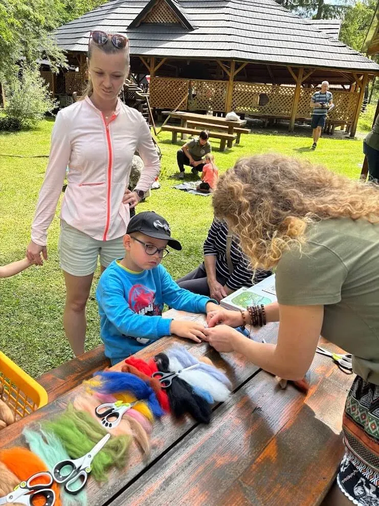 A child making a felt figure at an outdoor craft workshop, coloured wool and scissors spread across the table.
