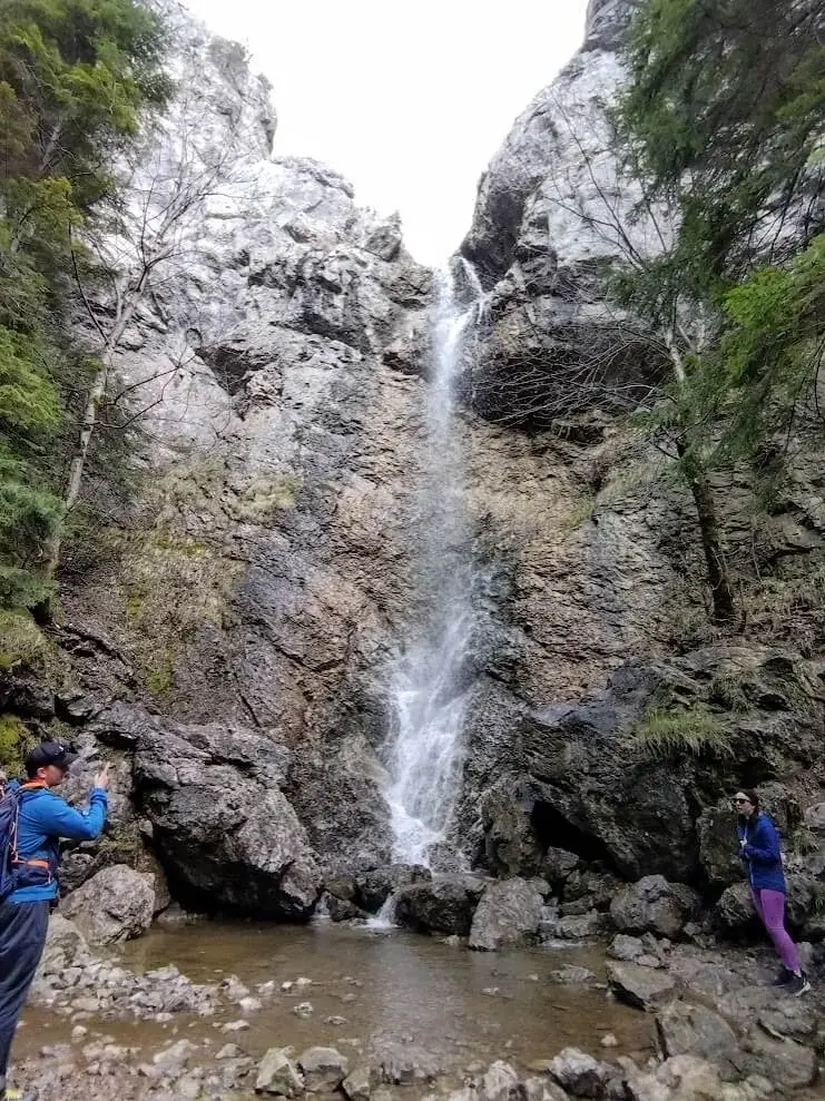 A waterfall falling down a cleft in the limestone cliffs of a Slovak gorge, visitors on the rocks below.