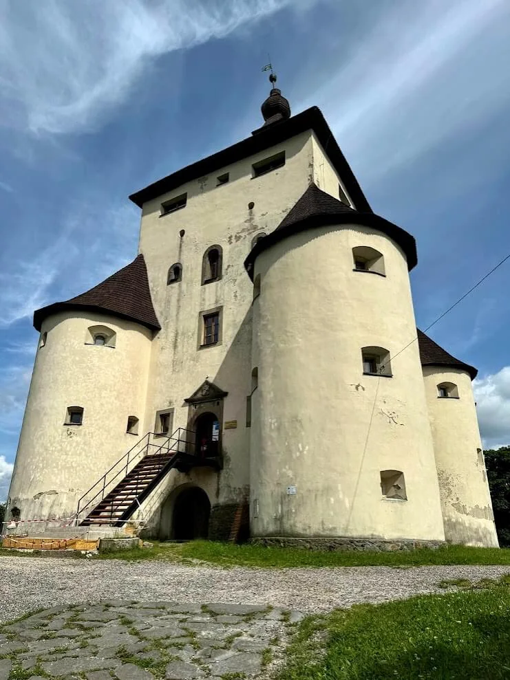 A white Renaissance castle with round corner bastions and shingled roofs standing above a grassy slope.