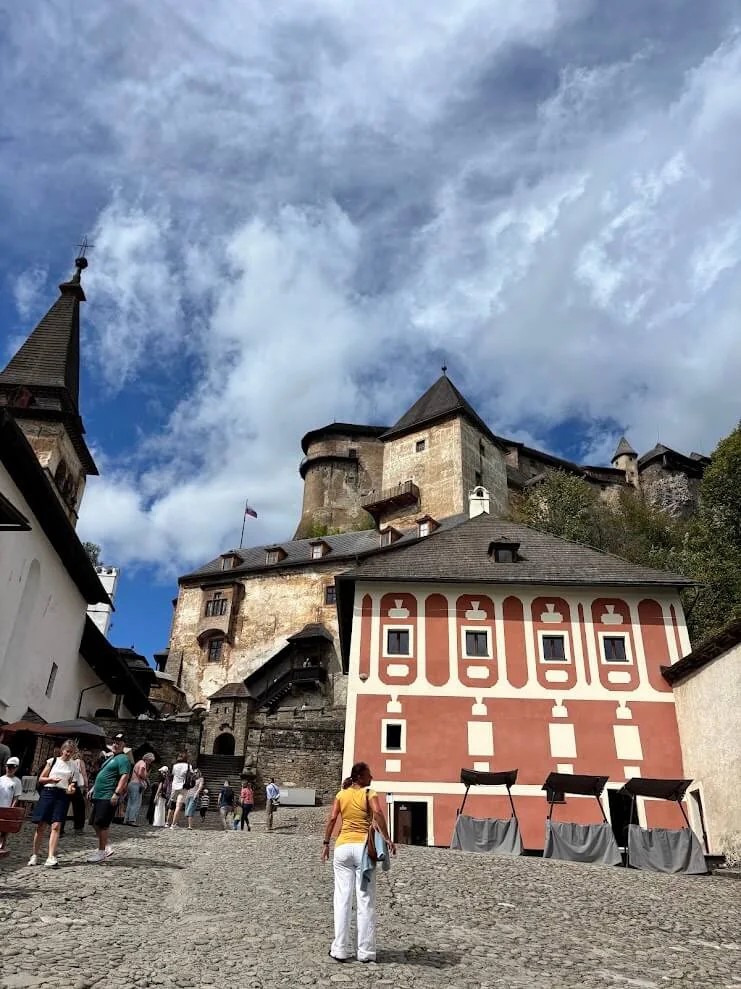 Visitors in the courtyard of Orava Castle, the red-and-white painted house below the fortress walls and towers.
