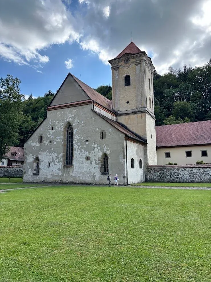 The church of the Red Monastery at Červený Kláštor, its baroque tower and tall Gothic windows above the lawn, wooded hills behind.