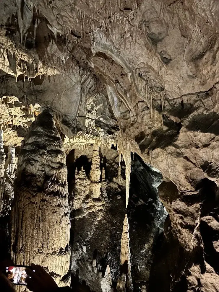 A tall stone column and dense stalactites lit inside the Demänovská Cave of Liberty, a visitor photographing from below.